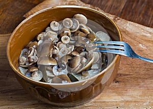 Marinated honey fungus in brown bowl on wooden table.
