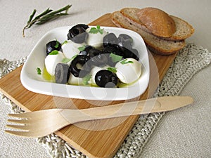 Marinated mozzarella with black olives, olive oil and mustard leaves