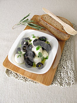 Marinated mozzarella with black olives, olive oil and mustard leaves