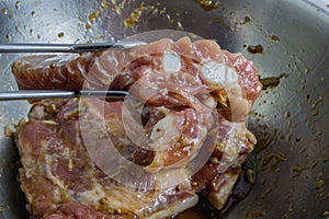 Marinated pork with herbs and sauce in a bowl and tongs.