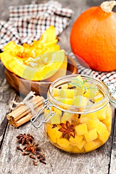 Marinated pumpkin dices in a glass container on a wooden table.