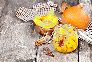 Marinated pumpkin dices in a glass container on a wooden table.