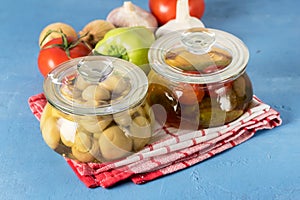 Marinated Tomatoes Cucumbers and Mushrooms in a Glass Jar Snacks with Pickled Vegetables on a Blue Background Napkin Horizontal