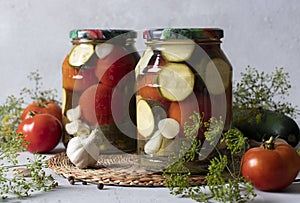 Marinated zucchini with tomatoes in two glass jars for the winter on a light background with fresh ingredients