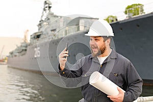 Marine assistant engineer holding VHF walkie talkie and papers near vessel in background.