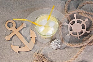 Marine attributes. A decorative, wooden anchor and helm next to a cold lemonade on the sand.