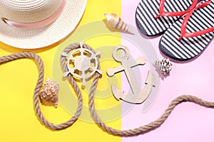 Marine paraphernalia and beach accessories. Wooden steering wheel and an anchor with a rope on a bright pink and yellow background