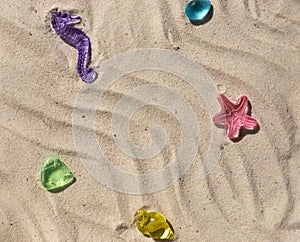 Marine transparent colorful figurines or kid's toys on the beach sand. Summer sea vacation concept background.