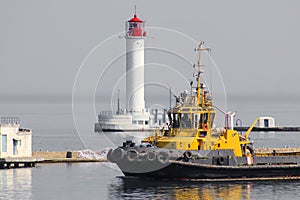 Marine tugboat coming out of harbor seaport on lighthouse background.