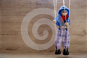 A marionette-clown doll hanging on thin threads on a wooden background