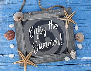 Maritime decoration with star fish, shells on blue weathered wood with slogan Enjoy the summe