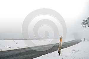 Marker post by a misty road in the winter