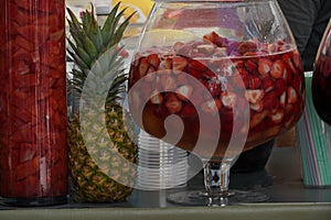Market stand with ananas and punch drinks. Serving bowl full of punch with strawberries and other various types of fruits.