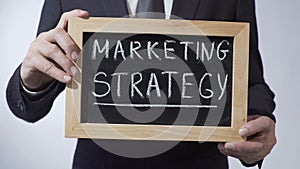 Marketing strategy written on blackboard, businessman holding sign, business