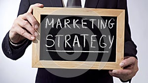 Marketing strategy written on blackboard, businessman holding sign, business