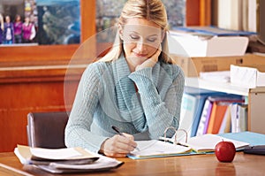 Marking homework. A young teacher marking exam papers in her office.