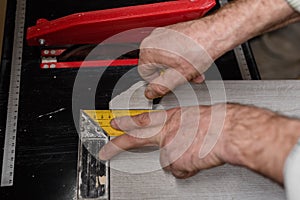 a marking the tiles with a yellow ruler and a pencil for cutting with an electric tile cutter