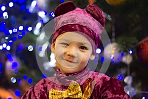 Marmalade bear. Emotional boy three years old in a purple bear costume on the background of a New Year tree and blue lanterns