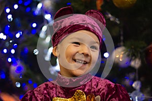 Marmalade bear. Emotional boy three years old in a purple bear costume on the background of a New Year tree and blue lanterns