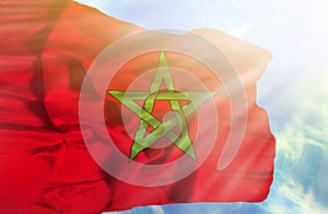 Marocco waving flag against blue sky with sunrays