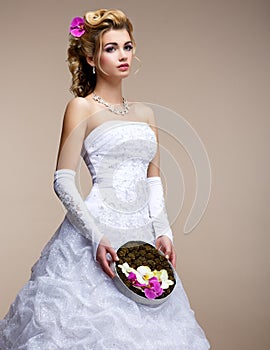 Marriage. Fashionable Bride Blonde in Bridal White Dress and Unusual Bouquet of Flowers