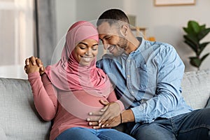 Married black muslim couple expecting baby cuddling on couch in living room