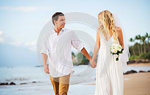 Married couple, bride and groom holding hands at sunset on beaut