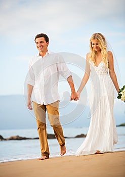 Married couple, bride and groom holding hands at sunset on beaut