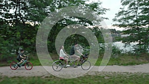 Married couple with a child rides a two-person tandem bike along the river bank