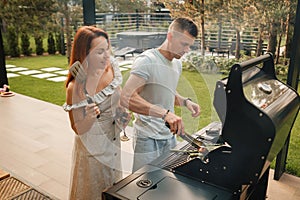 A married couple cooks grilled meat together on their terrace