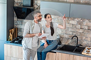married couple with digital tablet looking away in kitchen smart