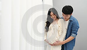 Married couple is expecting baby. man embraces his pregnant wife on window background