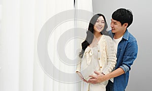 Married couple is expecting baby. man embracing and talking with his pregnant wife while looking view through the window