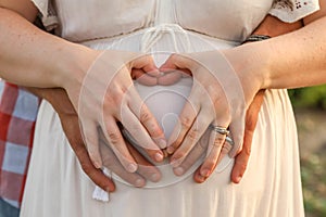 Married couple forming a heart shape with hands on the pregnant belly of the woman