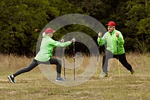 Married couple, happy middle age woman and man training with Scandinavian sticks in autumn forest, outdoors. Nordic