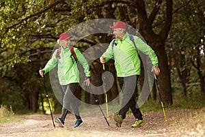 Married couple, happy middle age woman and man walking with Scandinavian sticks in autumn forest, outdoors. Nordic