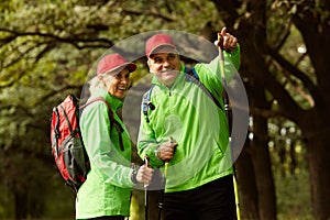 Married couple, happy middle age woman and man walking with Scandinavian sticks in autumn forest, outdoors. Nordic