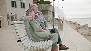 married couple having fun together sitting on a bench and enjoying the sea views on the embankment during a joint