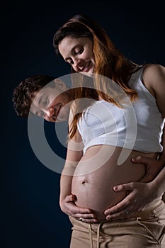 A married couple looks at the pregnancy belly with interest and they are happy because soon I will have a child. Hands