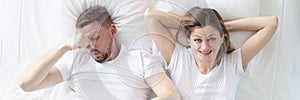 Married couple lying in bed. Man covering his nose with his hand