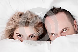 Married couple, man and woman, are lying in bed, hugging and sleeping on white bedding. Hiding their faces under blanket