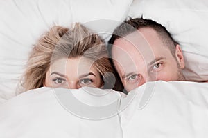 Married couple, man and woman, are lying in bed, hugging and sleeping on white bedding. Hiding their faces under blanket