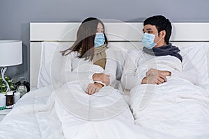 Married couple in medical masks talking together on bed, protection from coronavirus covid-19 pandemic concept