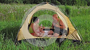 Married couple in an open tent playing cards on a sunny day in a clearing