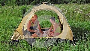 Married couple in an open tent playing cards on a sunny day in a clearing.