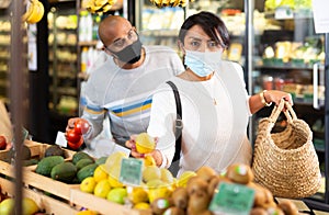 Married couple in protective mask choosing tomatoes at grocery store