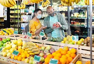 Married couple in protective mask choosing tomatoes at grocery store