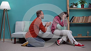 Married couple after a quarrel on the sofa. Husband asks his wife for forgiveness on his knees in the living room