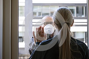 A married couple separated by Corona Covid-19 virus. She is quarantined indoors and he is outside wearing protective mask. They ar photo