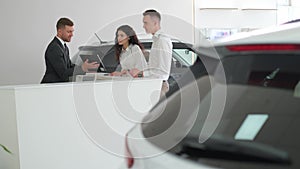 A married couple signs an order for the purchase of a car at a car dealership. Car salesman